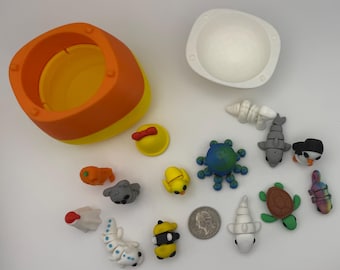 May include: An assortment of colorful, handcrafted clay figurines, including a shark, penguin, turtle, and octopus, alongside a yellow and orange container and a white bowl. A U.S. quarter is also present.
