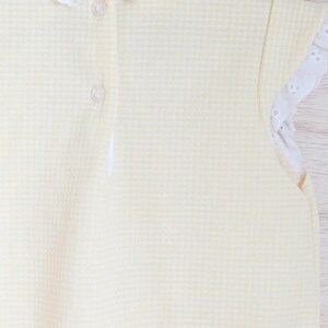Puede incluir: Un body de beb&eacute; amarillo y blanco con estampado de cuadros vichy, con cuello y ribetes de manga de encaje de ojal blanco. El body tiene dos botones transparentes en la espalda. La tela es un material suave y texturizado.