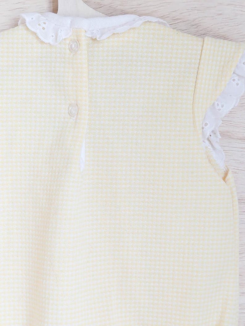 Puede incluir: Un body de beb&eacute; amarillo y blanco con estampado de cuadros vichy, con cuello y ribetes de manga de encaje de ojal blanco. El body tiene dos botones transparentes en la espalda. La tela es un material suave y texturizado.