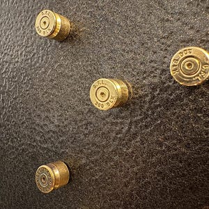 May include: Close-up of several brass bullet casings with the markings "G.F.L. 300 BLK" and "S&B 300 BLK" on a dark textured surface. The casings are arranged in a scattered pattern, showcasing their metallic sheen.
