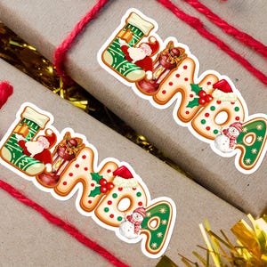 May include: Two gift-wrapped boxes with red twine, each decorated with a sticker spelling "LINDA" in a Christmas theme. The stickers include Santa Claus, a snowman, and a Christmas stocking.