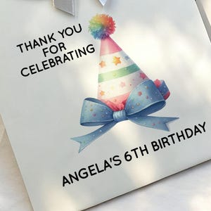 May include: White gift bag with a colorful party hat, blue bow, and text that reads "Thank You For Celebrating" and "Angela's 6th Birthday."