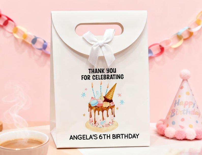 May include: White gift bag with a handle and a white bow. The bag features a birthday cake illustration with the text "THANK YOU FOR CELEBRATING" and "ANGELA'S 6TH BIRTHDAY". A party hat is visible in the background.