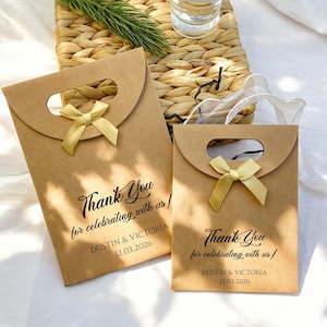 May include: Two brown paper gift bags with a curved top and a handle cutout. Each bag has a gold ribbon bow and the text "Thank You for celebrating with us!" with a date and names printed below.