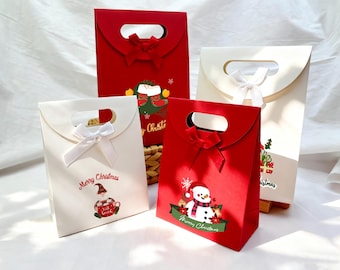 May include: Four Christmas-themed gift bags. Two are red, two are white. Each has a handle and a bow. The red bags feature a snowman and a Christmas elf graphic. The white bags have a gnome and gift graphic. Text reads "Merry Christmas."