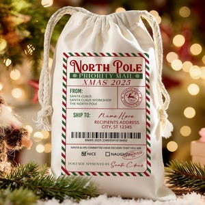 May include: A cream-colored drawstring gift bag with a festive North Pole Priority Mail label. The label features red and green borders, the text "XMAS 2025," and a barcode. The bag is decorated with a Santa Claus stamp and the text "Nice" is checked.