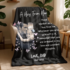 Könnte beinhalten: Schwarze Fleece-Decke mit dem Text "A Hug From Heaven" und "Love, Dad 1968-2025". Die Decke zeigt ein Foto eines Mannes und eines Kindes mit Schmetterlingsakzenten. Die Decke ist über einen Stuhl drapiert.