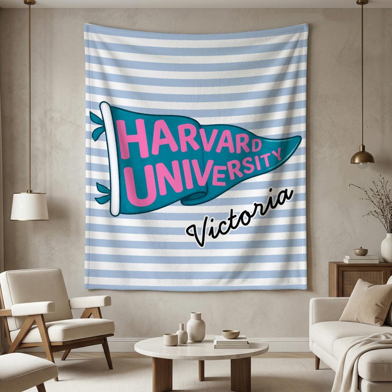 以下が含まれることがあります： 薄い青と白のストライプの背景の壁掛け。 ピンク色の「HARVARD UNIVERSITY」という文字が入ったターコイズ色のペナントが壁掛けの中央にあります。 ペナントの下には筆記体で「Victoria」という名前が書かれています。