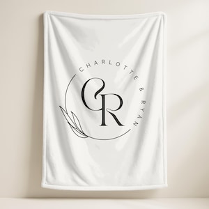 Könnte beinhalten: Weiße Decke mit einem schwarzen kreisförmigen Design mit den Namen "Charlotte & Ryan" und den Initialen "CR". Das Design beinhaltet ein Blatt und ist auf der Decke zentriert.