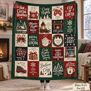 Puede incluir: Una manta grande y rectangular con un diseño de cuadrícula tipo patchwork con motivos invernales festivos en rojo, verde y crema. Cada cuadrado muestra ilustraciones estacionales como chocolate caliente, pinos, faroles y texto.