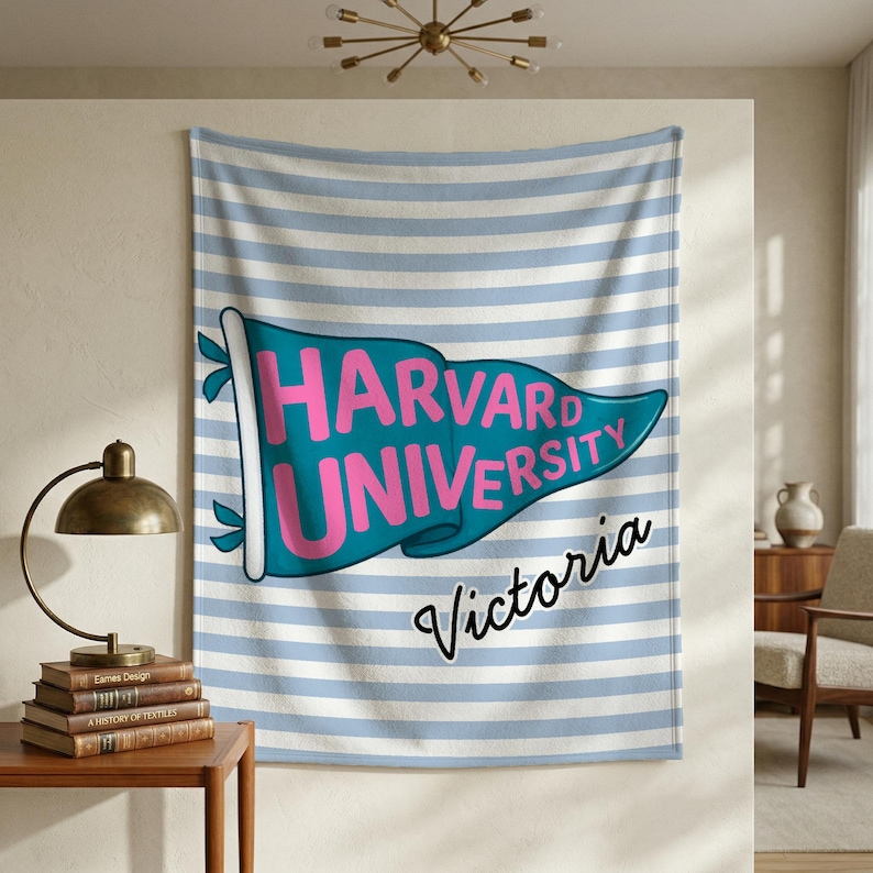 以下が含まれることがあります： 青と白のストライプの背景の壁掛け。 ピンク色の「HARVARD UNIVERSITY」という文字が入ったターコイズ色のペナントが壁掛けの中央にあります。 「Victoria」という言葉がペナントの下に筆記体で書かれています。