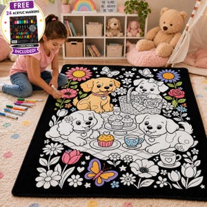 Pode incluir: Um tapete retangular de tecido preto com um design de contorno branco de três cachorros, flores, borboletas e uma cena de piquenique com cupcakes e chá. O tapete foi concebido para colorir e inclui 24 marcadores de tecido.