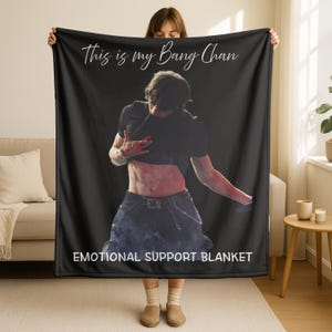 May include: Black blanket with white text reading "This is my Bang Chan" and "EMOTIONAL SUPPORT BLANKET". The blanket displays an image of a person in a black top and jeans.