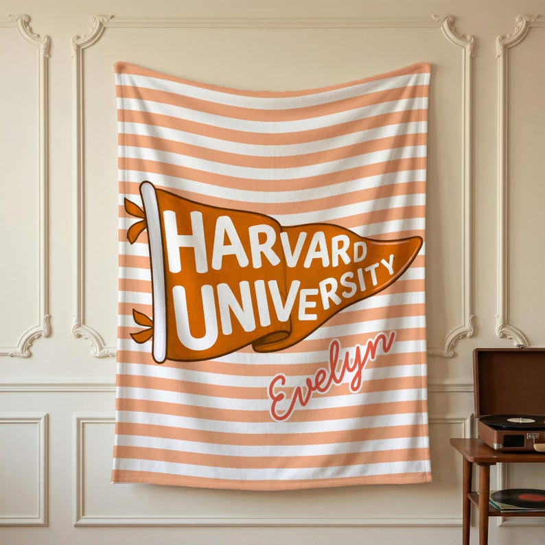 以下が含まれることがあります： オレンジと白の水平ストライプの長方形の毛布。 「HARVARD UNIVERSITY」の文字が白とオレンジで書かれたペナントが毛布の中央にあります。 ペナントの下には「Evelyn」という名前が筆記体で書かれています。