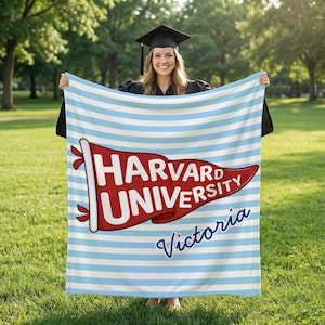 Op de afbeelding: Een blauw-wit gestreepte deken met een rode wimpel met de tekst "HARVARD UNIVERSITY" in witte letters en "Victoria" in blauwe letters. De deken wordt omhooggehouden voor een persoon die een afstudeerhoed en toga draagt.