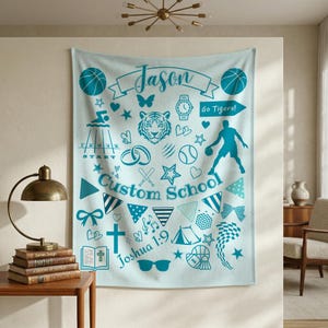 Puede incluir: Una manta escolar personalizada de color azul claro con varios gráficos turquesa, incluyendo balones de baloncesto, un tigre y los textos "Jason" y "Go Tigers!". La manta también presenta el texto "Custom School" y "Joshua 1:9".
