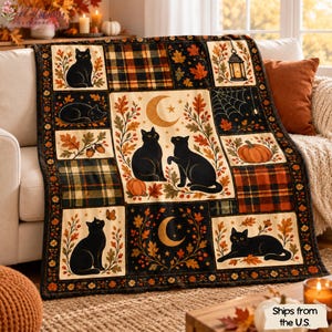 Op de afbeelding: Een rechthoekige plaid met een patchworkontwerp met zwarte katten, oranje pompoenen, herfstbladeren, ruitpatronen, een maansikkel, een spinnenweb en een lantaarn, afgebeeld tegen een donkere achtergrond met herfstkleuren.