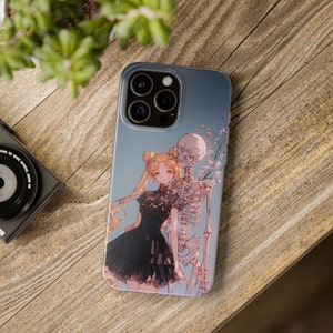 May include: A phone case featuring an anime-style illustration of a woman in a black dress and a skeleton, set against a blue sky background. The case is on a wooden surface, with a camera and plant visible.