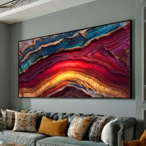 May include: Large framed abstract art print featuring a vibrant, layered design. The artwork showcases a spectrum of colors, including blues, reds, yellows, and golds, creating a visually striking and textured appearance. The piece is framed in a black border, suitable for home decor.