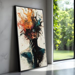 May include: Abstract art print featuring a figure with a burst of colorful paint above the head. The artwork uses a palette of orange, blue, and black against a white background. The framed print leans against a wall, showcasing the artwork's details.