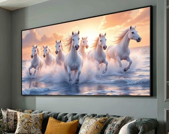 May include: A framed canvas print depicts seven white horses galloping through ocean waves under a sunset sky. The horses have flowing manes and tails, creating a sense of movement and freedom. The artwork is displayed above a gray sofa with decorative pillows.