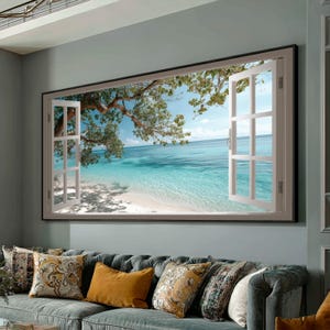 Puede incluir: Una obra de arte enmarcada que representa una ventana abierta con vistas a una playa tropical. El marco de la ventana es blanco, y la escena incluye agua turquesa, una playa de arena y un árbol con hojas verdes. La obra de arte está sobre un sofá azul con cojines decorativos.