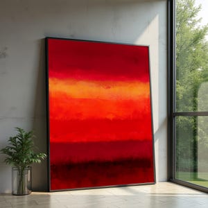 Puede incluir: Impresión artística abstracta con bandas horizontales superpuestas en rojo, naranja y negro. La obra de arte está enmarcada en un marco negro y se apoya contra una pared de hormigón. Una ventana con vistas a la vegetación está al lado.