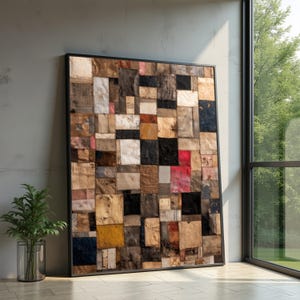 Può includere: Grande opera d'arte incorniciata con un design patchwork. L'opera è composta da quadrati di tessuto in tonalità marrone, beige, nero e rosso. La cornice nera contrasta con l'opera, appoggiata a un muro grigio vicino a una finestra.