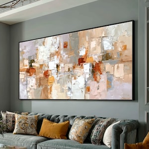 Könnte beinhalten: Abstraktes Ölgemälde auf Leinwand, rechteckig und in einem schwarzen Rahmen. Die Kunst verwendet eine Palette aus Weiß, Beige, Orange und Grau, aufgetragen in strukturierten Pinselstrichen. Das Gemälde hängt über einem grauen Sofa mit dekorativen Kissen.