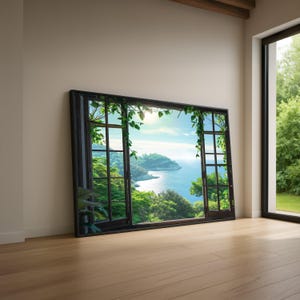 Op de afbeelding: Een groot ingelijst kunstwerk dat een kustlandschap toont door een zwart raamkozijn. Weelderig groen gebladerte en wijnranken sieren het frame, met een helderblauwe lucht en zee zichtbaar. Het kunstwerk leunt tegen een beige muur.