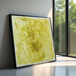 May include: Abstract art print with a black frame. The artwork features a textured, yellow and green design with linear and organic shapes. The piece is leaning against a white wall next to a window.