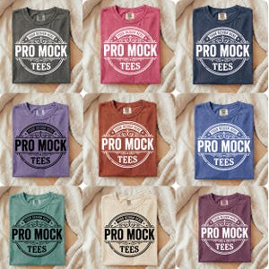May include: Nine folded t-shirts in various colours, including grey, red, navy, purple, rust, blue, teal, cream, and burgundy. Each shirt features the text "PRO MOCK TEES" in a circular design. The shirts are displayed on a neutral background.