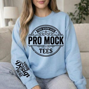 May include: A light blue sweatshirt with the text "PRO MOCK TEES" in a black circular design on the front. The sleeve has the text "YOUR DESIGN HERE" in a black script. The sweatshirt is a crew neck style.