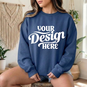 May include: A navy blue sweatshirt with the text "YOUR Design HERE" in white script. The sweatshirt is a crew neck style and appears to be made of a soft material. The model is wearing denim shorts.
