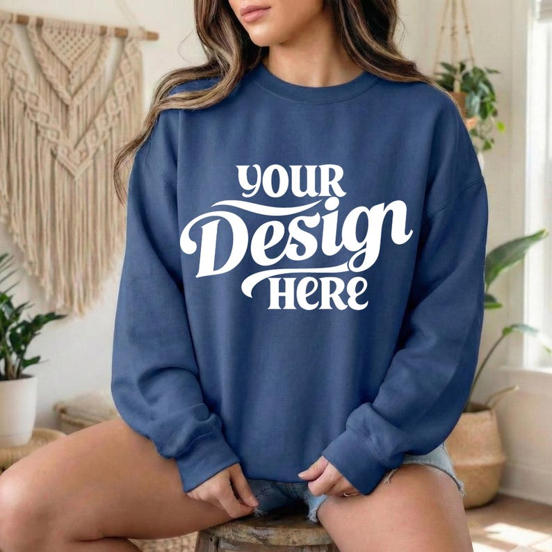 May include: A navy blue sweatshirt with the text "YOUR Design HERE" in white script. The sweatshirt is a crew neck style and appears to be made of a soft material. The model is wearing denim shorts.