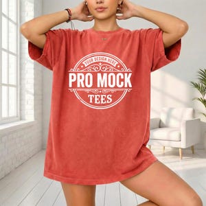 May include: A short-sleeved, coral-colored t-shirt with a large white circular graphic in the center. The graphic reads "YOUR DESIGN HERE" at the top, "PRO MOCK" in the middle, and "TEES" at the bottom. The shirt has a slightly faded appearance.