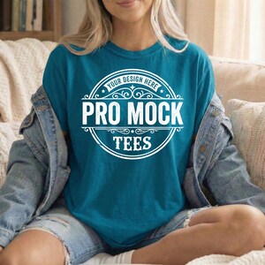 Peut inclure: T-shirt de couleur teal avec le texte "PRO MOCK TEES" dans un design circulaire blanc. Le t-shirt est de couleur unie et a un col rond. Les mots "YOUR DESIGN HERE" sont en haut du design.