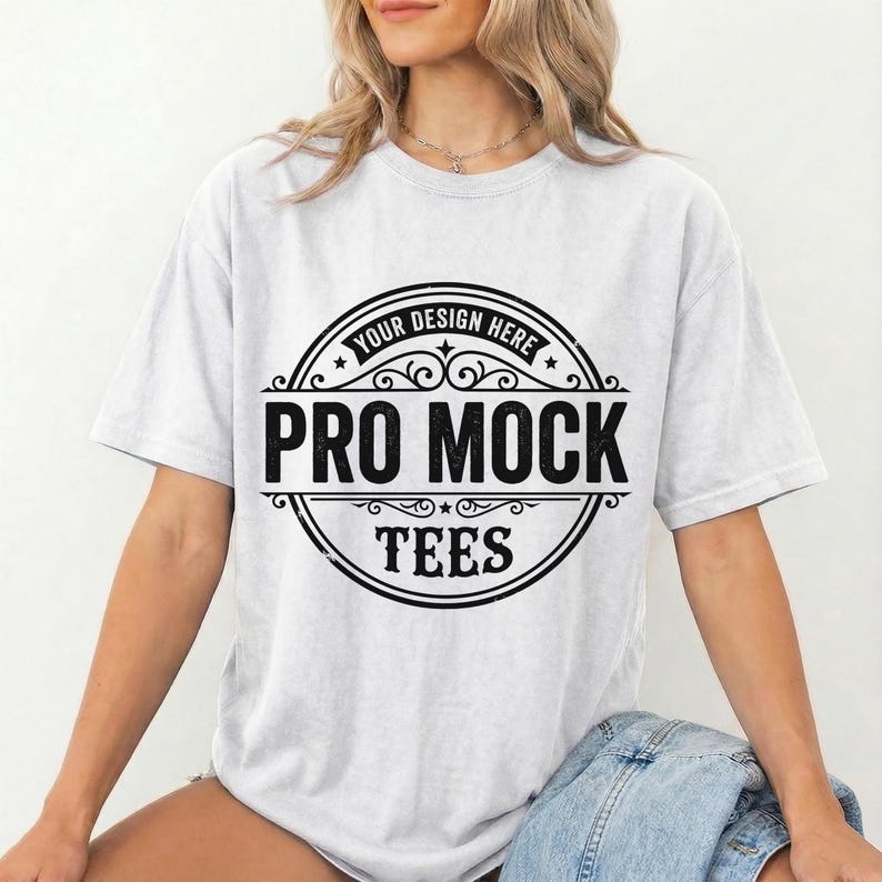 May include: A light gray t-shirt with the text "PRO MOCK TEES" in a black circular design. The design includes the words "YOUR DESIGN HERE" at the top. The shirt is short-sleeved and has a relaxed fit.