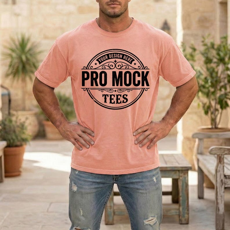 May include: A peach-colored t-shirt with the text "PRO MOCK TEES" in a black circular design. The shirt is short-sleeved and appears to be made of a soft material. The text "YOUR DESIGN HERE" is above the main text.