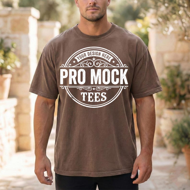 May include: A brown t-shirt with a round white graphic that reads "PRO MOCK TEES" in a stylized font. The text "YOUR DESIGN HERE" is arched above the main text. The shirt is short-sleeved and has a relaxed fit.