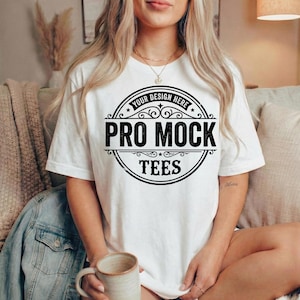 Peut inclure: T-shirt blanc avec un motif circulaire noir. Le texte "Your Design Here" est en haut et "Pro Mock Tees" au centre. Le mod&egrave;le porte un mug. Le t-shirt est de style d&eacute;contract&eacute;.