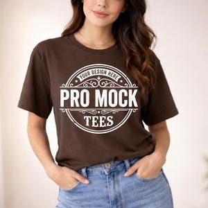 May include: A brown t-shirt with a white circular logo that reads "PRO MOCK TEES". The logo also includes the text "YOUR DESIGN HERE" at the top. The model is wearing blue jeans.