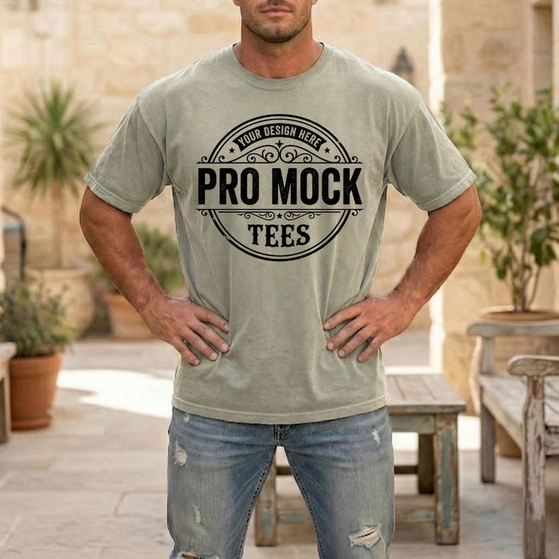 May include: A light green t-shirt with a crew neck and short sleeves. The shirt features a black circular design with the text "YOUR DESIGN HERE" at the top and "PRO MOCK TEES" in the center. The model is wearing blue jeans.