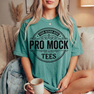 May include: Teal-colored t-shirt with a black graphic that reads "PRO MOCK TEES" in a circular design. The shirt has short sleeves and a relaxed fit. The text "YOUR DESIGN HERE" is above the main text.