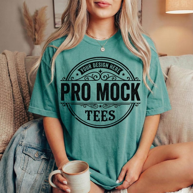 May include: Teal-colored t-shirt with a black graphic that reads "PRO MOCK TEES" in a circular design. The shirt has short sleeves and a relaxed fit. The text "YOUR DESIGN HERE" is above the main text.