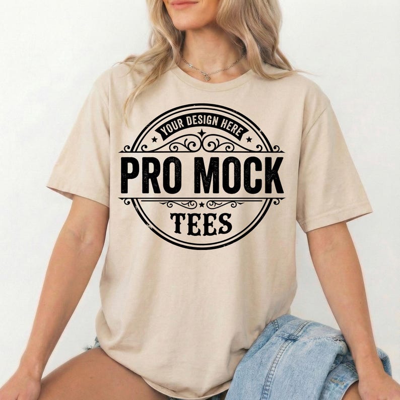 Peut inclure: T-shirt beige avec un motif circulaire noir. Le motif comprend le texte "YOUR DESIGN HERE" en haut et "PRO MOCK TEES" en lettres noires en gras. Le t-shirt a des manches courtes et un col rond.