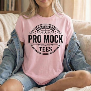 Peut inclure: T-shirt rose clair avec l'inscription "PRO MOCK TEES" dans un motif circulaire noir. Les mots "YOUR DESIGN HERE" sont en haut du motif. La personne porte une veste en jean bleu clair.