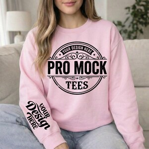 May include: A light pink sweatshirt with the text "PRO MOCK TEES" in a black circular design on the front. The sleeve has the text "YOUR DESIGN HERE" in black. The sweatshirt is a crew neck style.