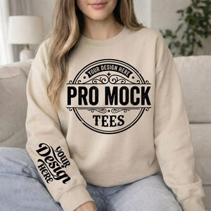 May include: A beige sweatshirt with the text "PRO MOCK TEES" in a black circular design on the front. The sleeve has the text "YOUR DESIGN HERE" in a black script. The sweatshirt is a neutral color.