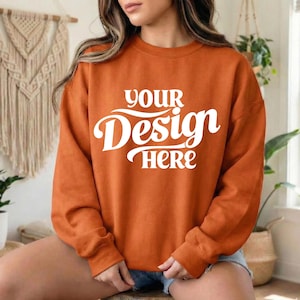 May include: An orange sweatshirt with the text "YOUR Design HERE" in white script. The long-sleeved top is a solid color and appears to be made of a soft material. The sweatshirt is a casual style.